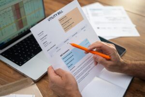 Close-up of a man calculating utility bills with laptop and documents on a wooden table.